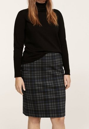 Frau, die einen schwarzen Rollkragenpullover und einen knieumspielenden Bleistiftrock in dunklem Karo mit Blau- und Grautönen trägt.