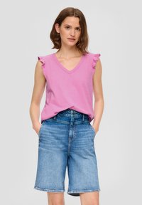 Różowa bezrękawnik z dekoltem w kształcie litery V i falbaniastymi ramionami, zestawiony z niebieskimi szortami z wysokim stanem, o luźnym kroju z bocznymi kieszeniami.