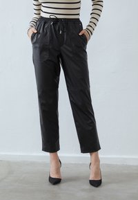Pantalones de cuero negro con cintura elástica y cordón de ajuste, que cuentan con bolsillos laterales y un diseño ajustado. Textura suave y longitud recortada.