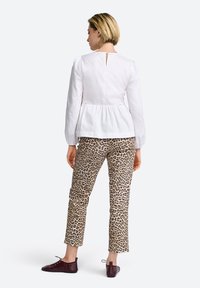 Top peplum bianco con maniche lunghe, dettaglio a chiave sulla schiena, abbinato a pantaloni beige con stampa leopardata e scarpe flat bordeaux.