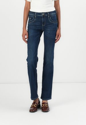 Dunkelblaue Jeans mit geradem Bein, fünf Taschen und Knopfverschluss. Das Material hat eine glatte Denim-Textur. Getragen mit braunen Slippern.