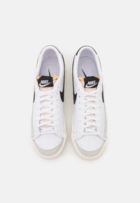 Bílé sportovní tenisky s černými akcenty, se semišovým špičkovým okrajem, světle růžovými tkaničkami a klasickou gumovou podrážkou. Logo Nike na jazyku.