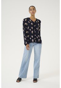 Navy blouse with pink floral pattern, long sleeves, and a button-down front, paired with light blue wide-leg jeans and black heeled sandals.