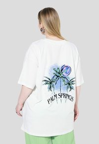 Camiseta blanca de gran tamaño con un diseño colorido de palmera y el texto "PALM SPRINGS" en la parte posterior, hecha de suave tejido de algodón.
