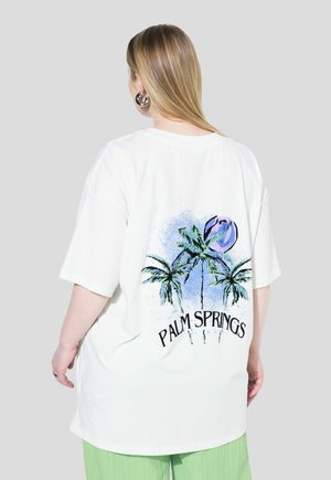 T-shirt oversize bianco con un design colorato di palma e il testo "PALM SPRINGS" sul retro, realizzato in morbido cotone.