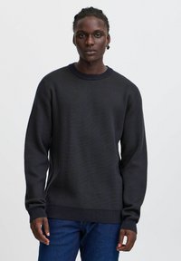 Maglione lavorato a maglia blu scuro con un design texturizzato, scollo a girocollo e maniche lunghe. Polsini e orlo a coste. Abbinato a jeans blu.