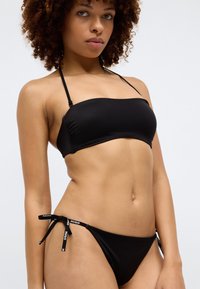 Μαύρο μπικίνι σετ από απαλό ύφασμα. Το τοπ διαθέτει αδιάβροχο σχέδιο, ενώ τα σλιπ έχουν δέσιμο στα πλάγια με ετικέτες της μάρκας.