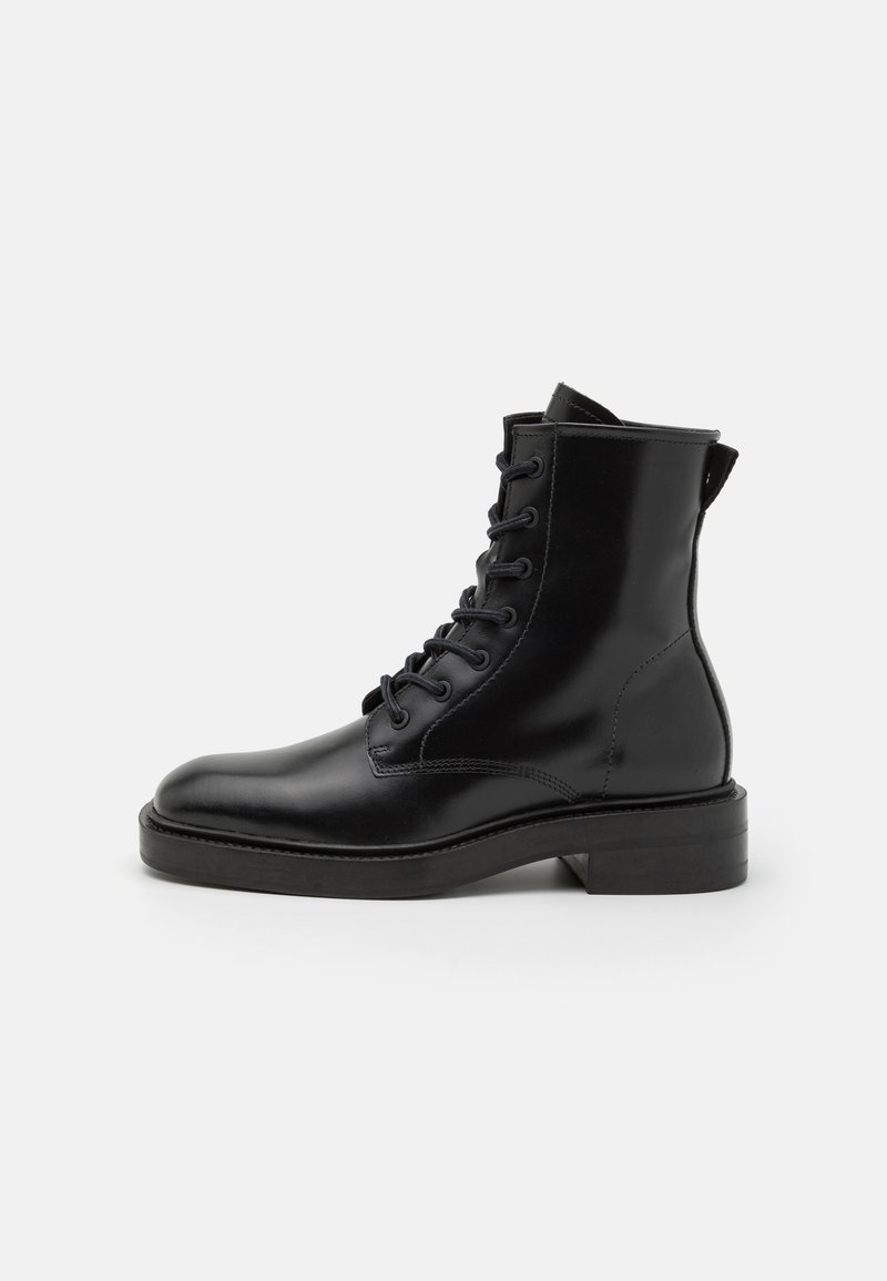 Bottine en cuir noir avec un laçage à l'avant, bout rond et petit talon bloc sur un fond blanc.