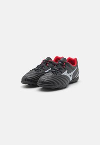 Scarpe da ginnastica nere con un upper in pelle testurizzata, caratterizzate da accenti e lacci rossi e un logo argentato sul lato. Progettate per gli sport.