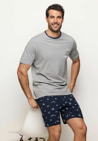 Maglietta in cotone grigia con colletto blu navy, caratterizzata da una piccola grafica sul lato sinistro del petto; abbinata a pantaloni corti blu navy decorati con motivi di vela bianchi.