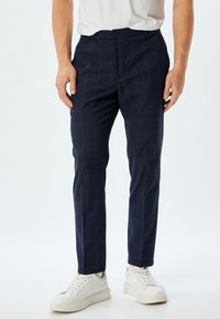 Marineblauwe geruite broek van soepel materiaal, met een slim fit, knoopsluiting, zijzakken en gedragen met witte sneakers.