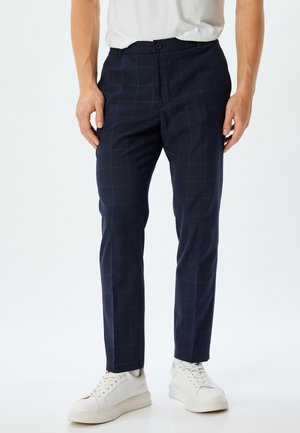 Navy checkered trousers made of smooth fabric, featuring a slim fit, button closure, side pockets, and paired with white sneakers.
