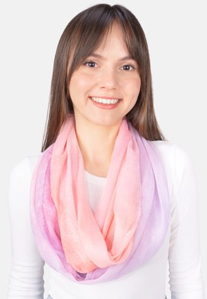 Junge Frau mit langem braunem Haar, lächelnd, trägt ein weißes Oberteil und einen sanften Schal mit Farbverlauf von Rosa zu Lavendel um den Hals.