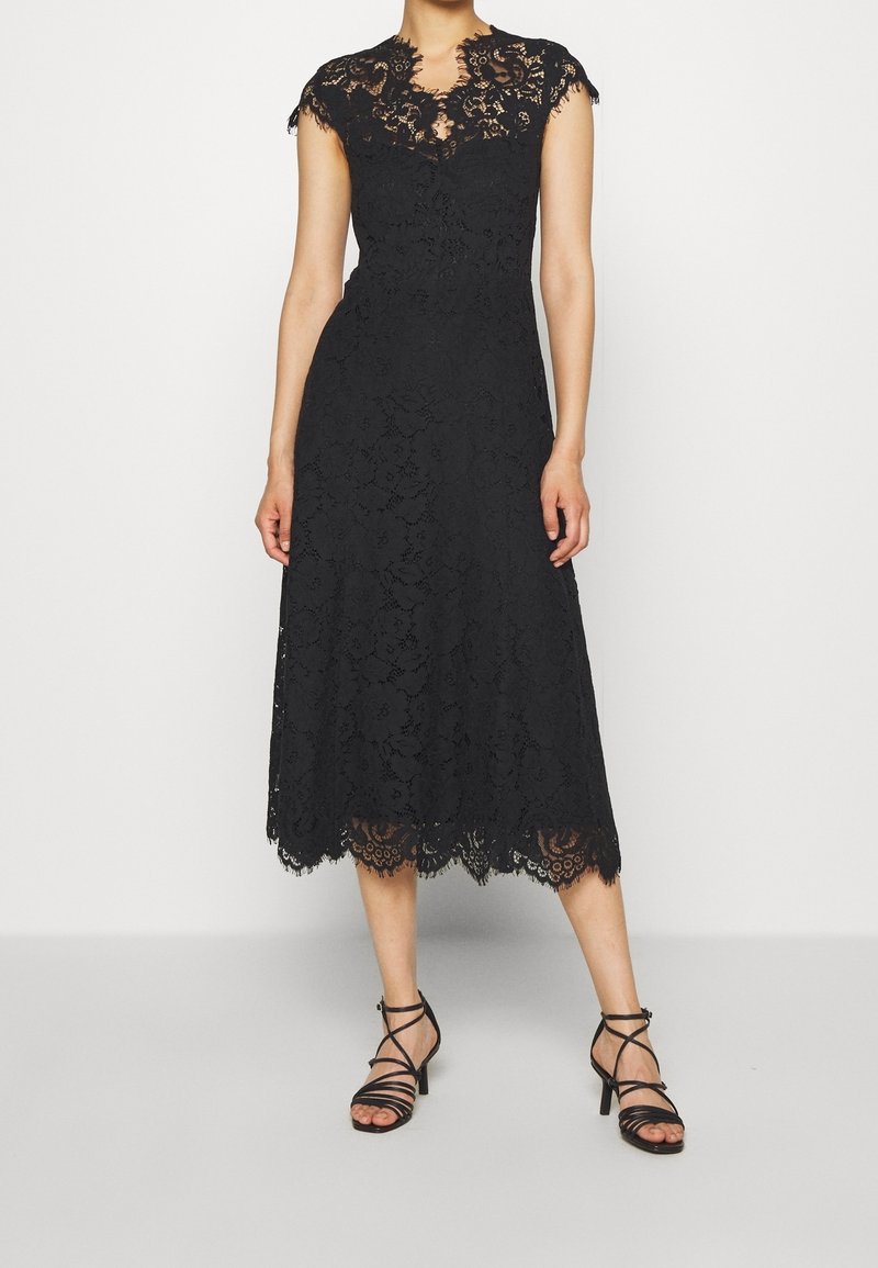 Robe midi en dentelle noire avec manches courtes et ourlet festonné, portée avec des sandales à talons noires à brides fines.