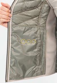 Wasserabweisendes, winddichtes Innenfutter der Jacke in hellgrün, mit gestepptem Muster und Symbolen, die die Materialeigenschaften anzeigen. Mit Reißverschlussöffnung.