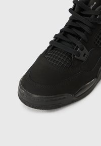 Μαύρο αθλητικό παπούτσι με πάνελ από δίχτυ και χοντρές κορδόνια, εστιασμένο στις λεπτομέρειες της μύτης και του μπροστινού μέρους σε απλό φόντο.