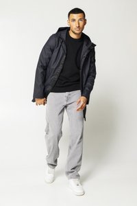 Black waterproof jacket with a hood, grey sweater, light grey jeans, and white sneakers; features zip and snap closures.