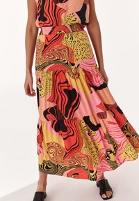 Jupe maxi colorée en tissu léger avec de grands motifs tourbillonnants de rouge, rose, jaune et noir. Design à volants avec une taille élastique.