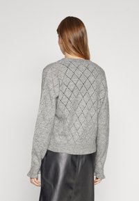 Gray knitted sweater with a diamond pattern, ribbed cuffs, and hem. Worn over a black textured skirt.