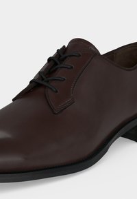 Gros plan d'une chaussure habillée en cuir marron foncé poli avec des lacets noirs et un petit talon noir.