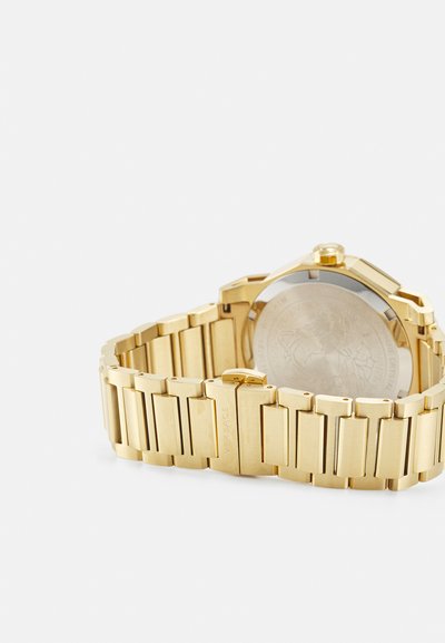 Gold metal watch with a rectangular case and linked bracelet. Features polished and brushed finishes with a circular, textured back.