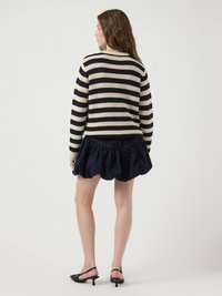 Maglione a righe in crema e nero, abbinato a una gonna blu scuro con volants. Tacchi slingback neri completano l'outfit.