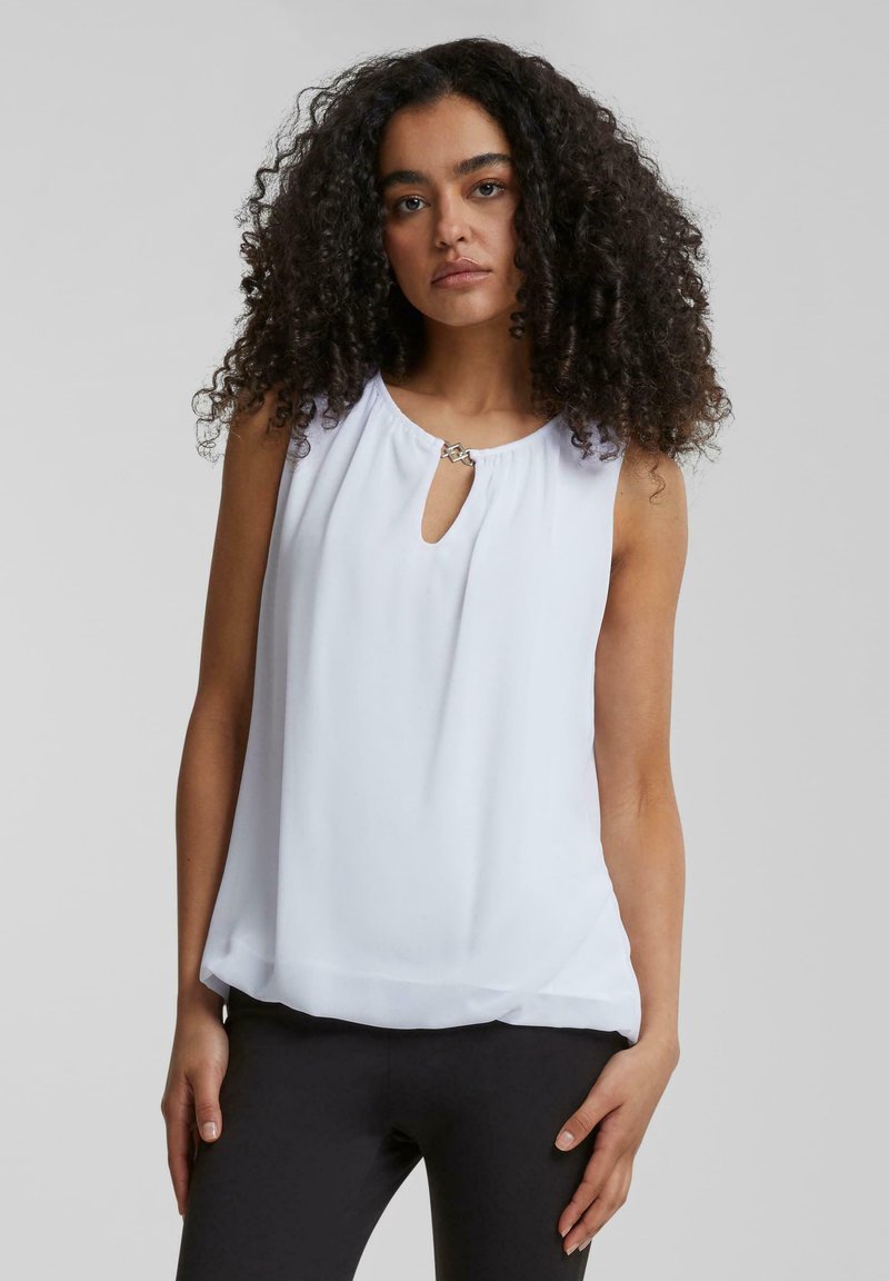 White sleeveless top with a round neckline and small keyhole detail, featuring a decorative metal accent. Smooth fabric with a loose fit.