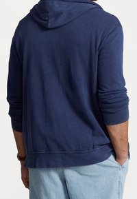 Marinblå hoodie i mjukt tyg med långa ärmar och dragsko i huvan. Har ribbad i nederkanten och ärmarna, avslappnad passform.