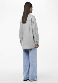 Oversized gray denim shirt features buttoned cuffs and back yoke. Paired with light blue wide-leg jeans, creating a casual outfit.