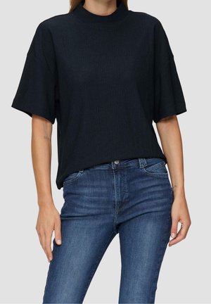 Czarna prążkowana bluzka z krótkim rękawem o wysokim dekolcie, w połączeniu z niebieskimi obcisłymi dżinsami. Materiał ma teksturowane wykończenie.