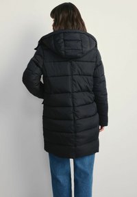 Czarna puchowa kurtka z kapturem, z pikowanym wzorem, pionowymi szwami i długością do połowy uda, w połączeniu z niebieskimi spodniami typu wide-leg.