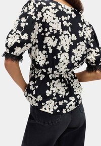 Blusa nera a fiori con fiori bianchi e rosa chiaro. Presenta maniche corte a sbuffo, bordi in pizzo e una cintura elastica per un look aderente.