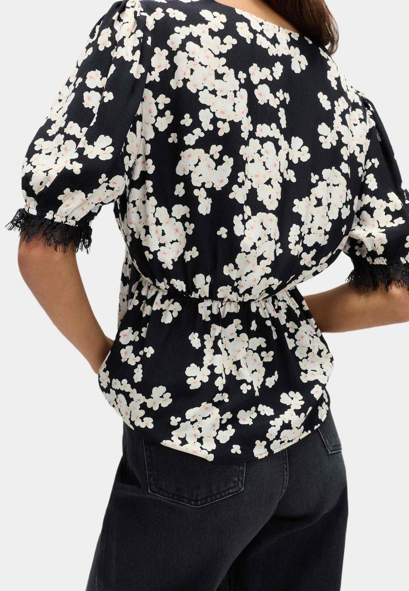 Blusa nera a fiori con fiori bianchi e rosa chiaro. Presenta maniche corte a sbuffo, bordi in pizzo e una cintura elastica per un look aderente.