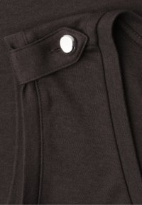 Tissu marron foncé en gros plan montrant une sangle cousue avec un bouton-pression argenté brillant et des détails de bord plié.