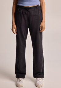 Black wide-leg sweatpants with an elastic waistband and drawstring detail, made of soft fabric. Paired with white sneakers.