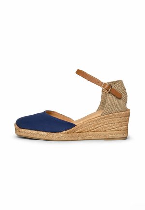 Zapato espadrille con cuña, parte frontal de tela azul marino, tacón de yute trenzado, cubre tobillo tejido y correa de hebilla ajustable en color marrón claro.