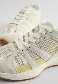Baskets de sport de couleur claire avec une tige en maille et en cuir suédé, dotées de lacets, d'une semelle en caoutchouc et d'accents texturés pour une meilleure adhérence et un bon maintien.