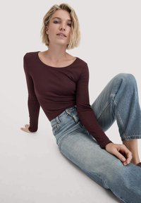 Bordeaux lange mouw top gecombineerd met lichtblauwe high-waisted jeans, met een klassiek snit en zachte, gladde stof.