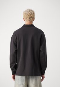 Zwarte lange mouw polo met kraag, met een relaxte pasvorm en zachte textuur, gecombineerd met lichte denim kortebroeken.
