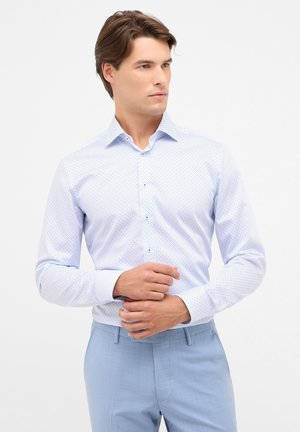 Lichtblauw overhemd met een wit stippenpatroon, met een button-down kraag en lange mouwen. Draag het met lichtblauwe broek.