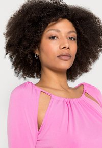 T-shirt de mangas longas rosa com decote franzido, detalhes de ombros recortados e textura suave. Apresenta um ajuste descontraído e um acabamento de tecido liso.