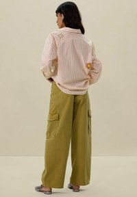 Chemise rayée aux douces teintes pastel avec broderie de soleil et d'étoiles, associée à un pantalon cargo vert olive avec poches latérales et une coupe décontractée.