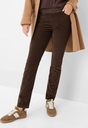 Bruine corduroy broek met een slim fit ontwerp en elastische tailleband, gecombineerd met bruine suède sneakers met witte veters en accenten.