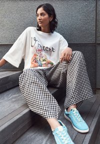 T-shirt oversize blanc avec un motif floral, associé à un pantalon large à carreaux noir et blanc et des baskets bleu clair.