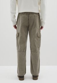 Kaki cargobroek van ribfluweel met een ontspannen pasvorm, voorzien van zijzakken en gestikte accenten, gedragen met bruine schoenen.