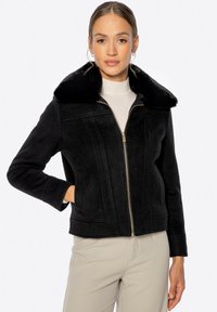 Chaqueta negra con cremallera y cuello de piel sintética. Presenta costuras estructuradas, mangas largas y bolsillos laterales. Está hecha de un material suave y texturizado.