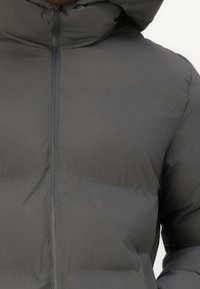 Polstret grå jakke med hætte, udstyret med en fuld lynlås og glat tekstur. Stoffet har en mat finish med en let glans.