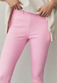 Roze denim jeans met een slim fit, voorzien van een hoge tailleband, een standaard vijf-pocket ontwerp en subtiele stiksels. De textuur lijkt glad.