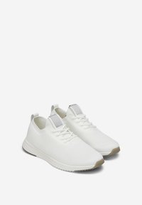 Chaussures de sport blanches en tissu mesh respirant avec une surface texturée. Dotées d'un col de cheville rembourré et d'une semelle en caoutchouc gris clair.