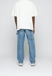 T-shirt blanc oversize à col rond, associé à un jean ample bleu clair avec une poche latérale et un patch en denim plus foncé.